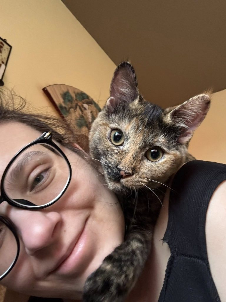 Young woman lying down with kitty on her shoulder.